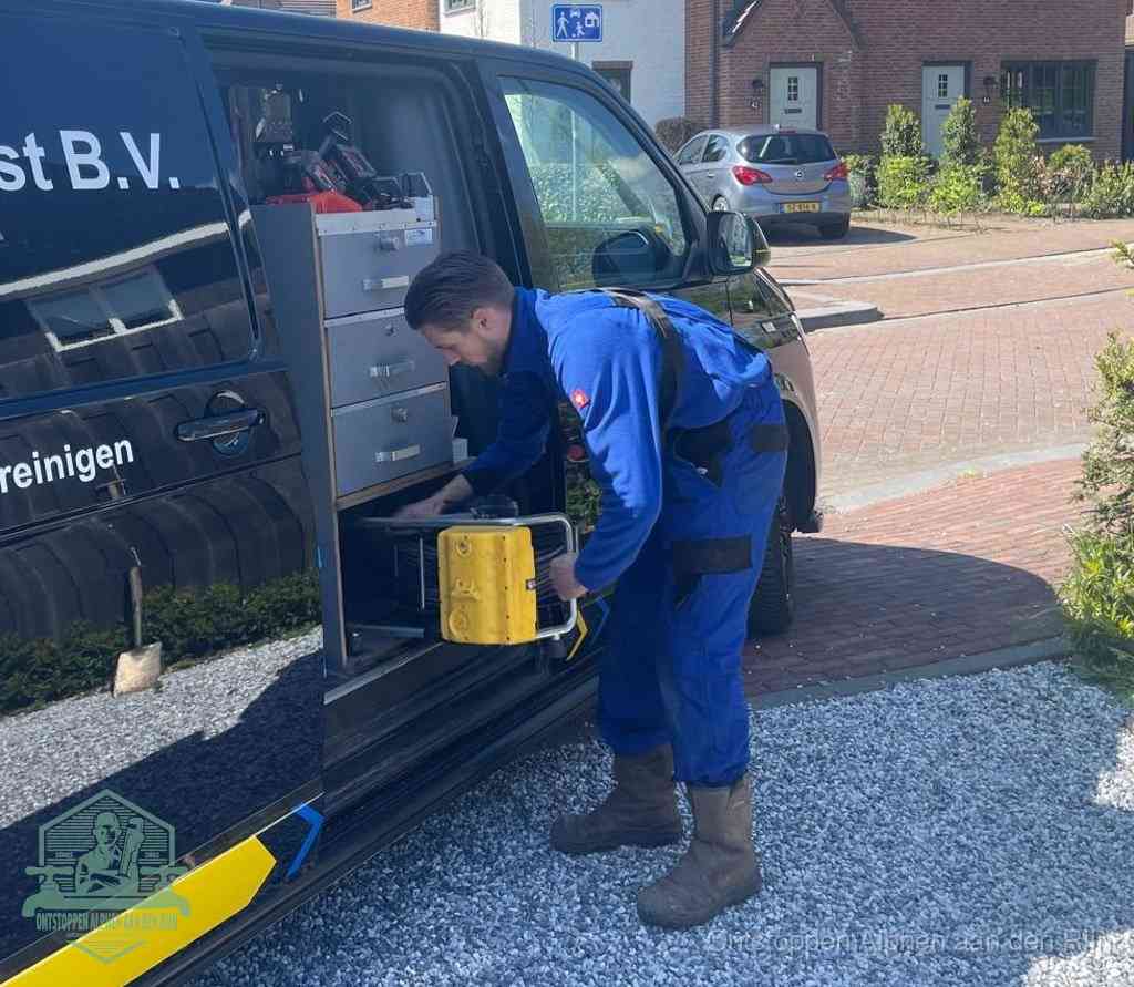 Een monteur pakt buiten op de oprit gereedschap uit de bedrijfsbus, het moment om een professional in te schakelen voor een verstopte afvoer in Alphen aan den Rijn