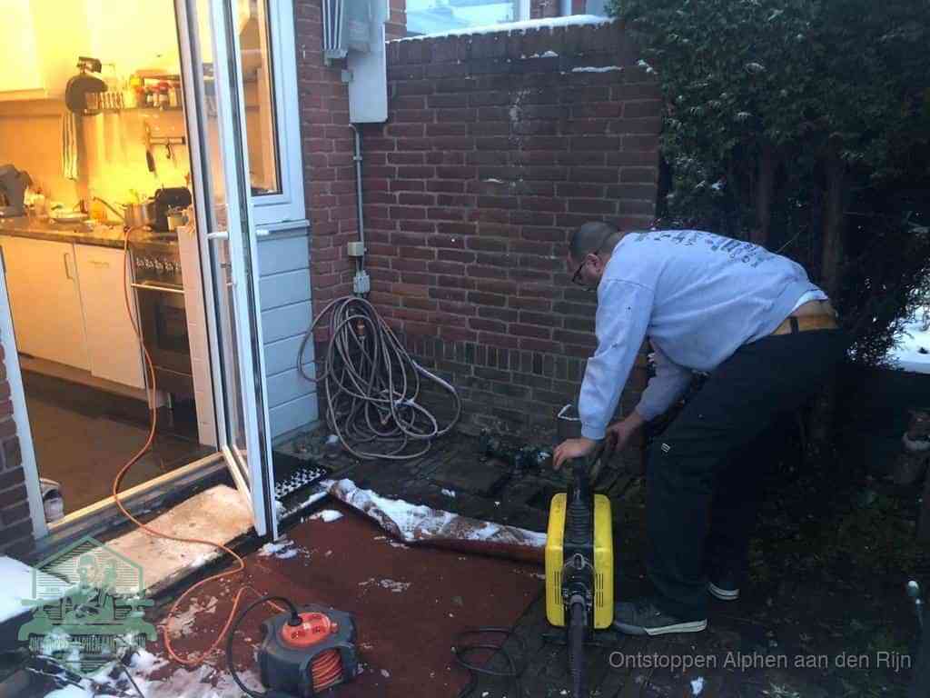 Een monteur werkt buiten bij een open riool-/grondput met een elektrische ontstoppingsmachine om een verborgen afvoerprobleem op te sporen in Alphen aan den Rijn