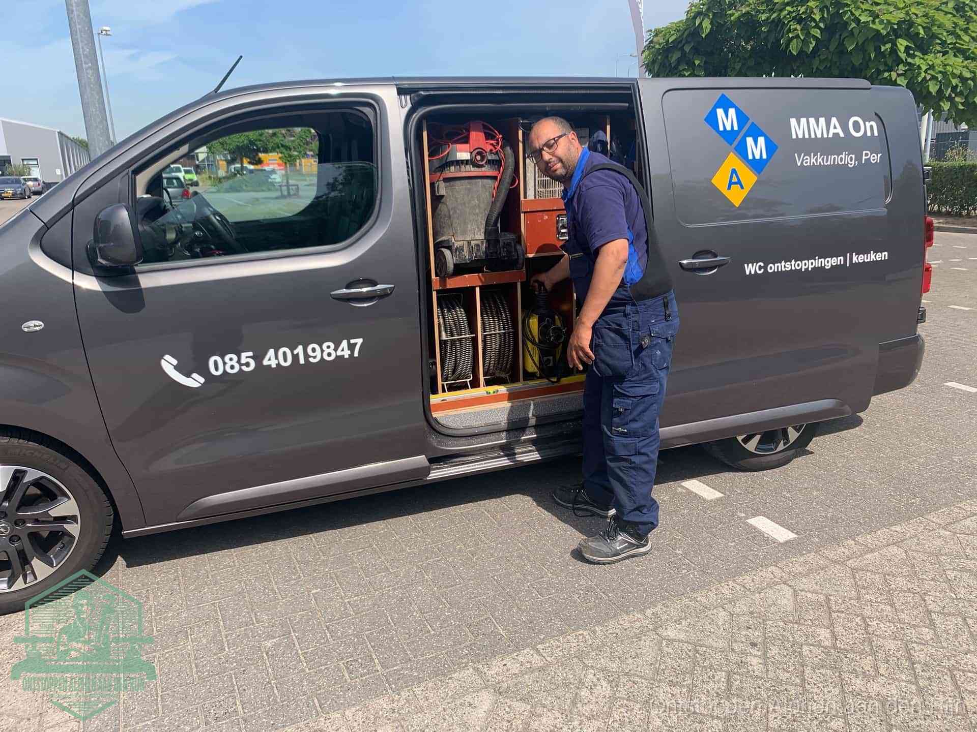 Een monteur bij de open schuifdeur van zijn bedrijfsbus op een parkeerplaats, klaar om de oorzaak van terugkerende afvoerverstoppingen aan te pakken in Alphen aan den Rijn