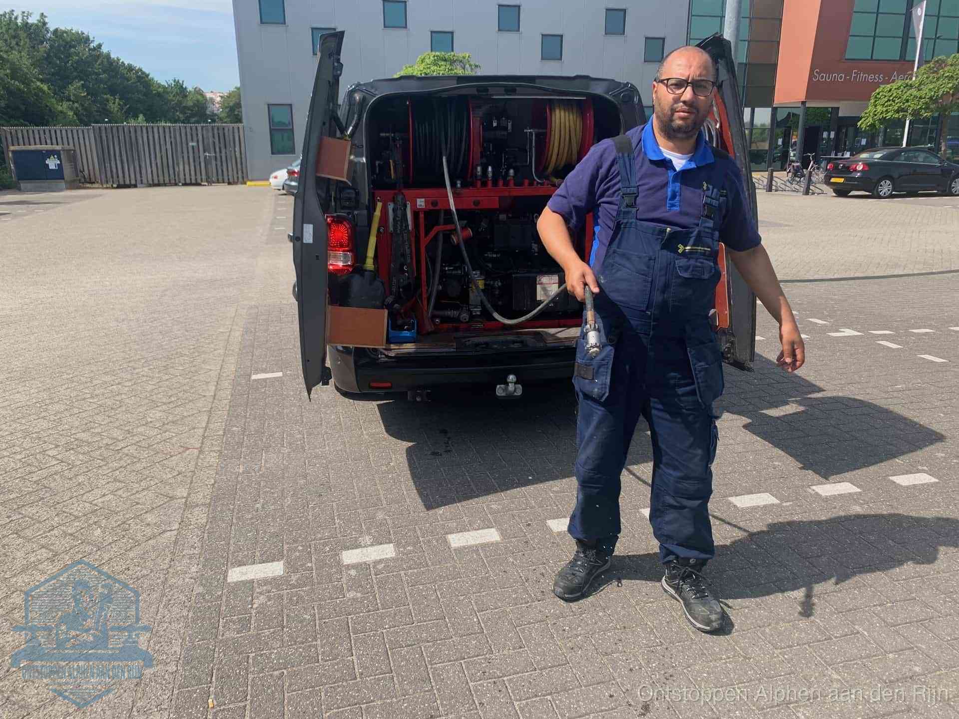 Een monteur bij zijn bestelbus met een hogedruk- en rioolreinigingsunit, klaar om de oorzaak van terugkerende wc-verstoppingen aan te pakken in Alphen aan den Rijn