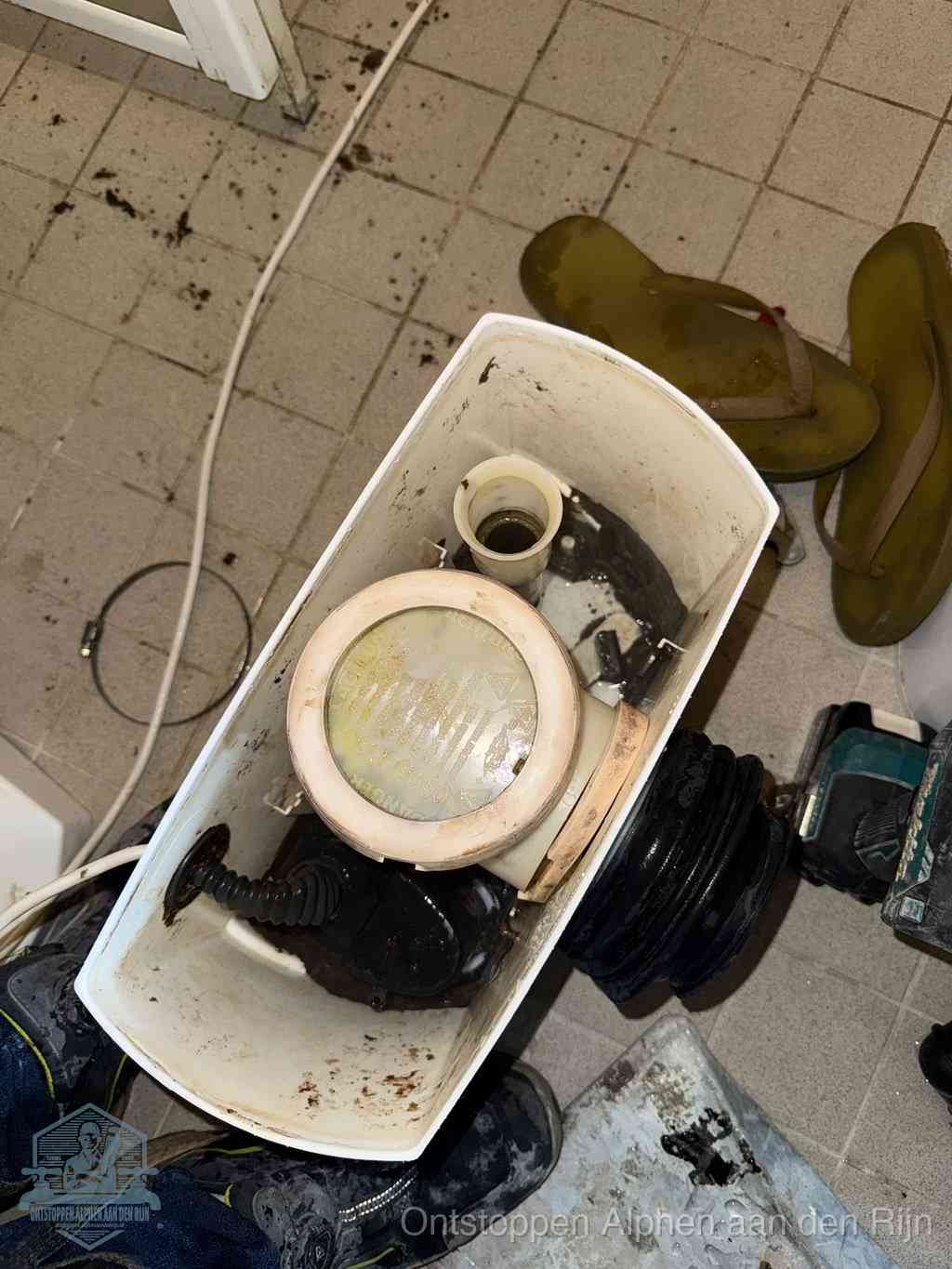 Een gedemonteerde toiletpot op de vloer met ontstoppingsveer en gereedschap ernaast, het verwijderen van een vastzittend voorwerp uit de wc in Alphen aan den Rijn