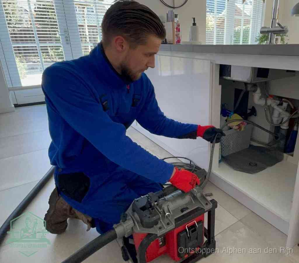 Een monteur met rode handschoenen knielt in een keuken en voert een elektrische ontstoppingsveer in tijdens het professioneel afvoer ontstoppen in Alphen aan den Rijn
